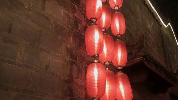 中国寺庙的底部到近距离的石墙和阳台在晚上点燃的红灯笼悬挂在屋顶的柱子上照亮灯光传统装饰东方节日庆典