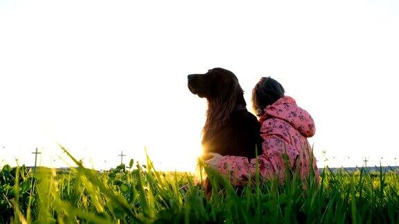 日落时分一个女人抱着一只狗一个小女孩抱着一只宠物坐在草地上在大自然中放松