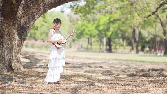 年轻迷人的女子在公园里弹吉他