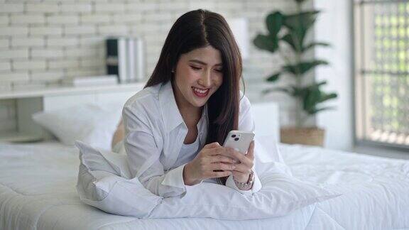 微笑的亚洲女性在床上放松地使用智能手机