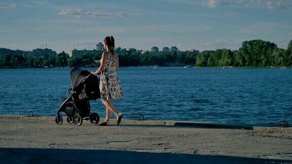 年轻漂亮的妈妈穿着衣服推着婴儿车在河边散步