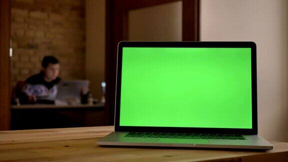 绿色屏幕的特写笔记本电脑躺在室内办公室的桌子上商人在模糊的背景下工作