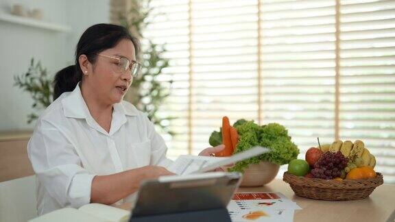 一名亚洲成年女性正在通过平板电脑向观众在线介绍蔬菜和水果的营养