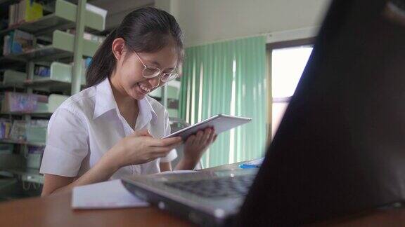 亚洲大学生女孩读书工作和网上购物与笔记本电脑和智能手机在公共图书馆做她的作业