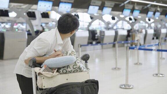 一名亚洲男子拿着行李在机场候机柜台打呵欠