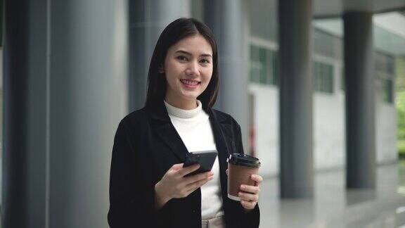 年轻优雅的亚洲忙碌的商务女性穿着西装拿着手机和一杯咖啡