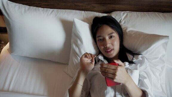 年轻的亚洲妇女躺在床上使用手机