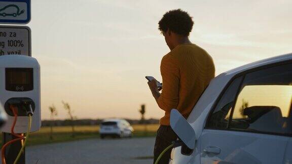 日落时分一名年轻的黑白混血男子在停车场给他的电动汽车充电