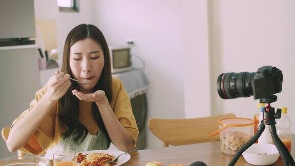 年轻的微笑美丽的女性影响力美食博主拍摄视频教程一边在家里的厨房吃意大利面社交媒体影响者