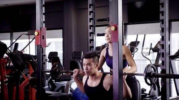 年轻的亚洲肌肉男子举起杠铃下蹲在健身房生活方式运动和健美