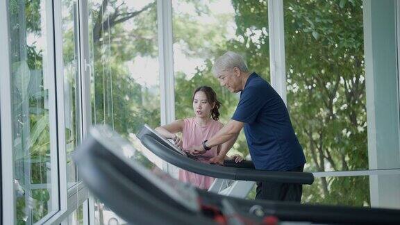 在健身房里一位老人在教练的帮助下使用跑步机