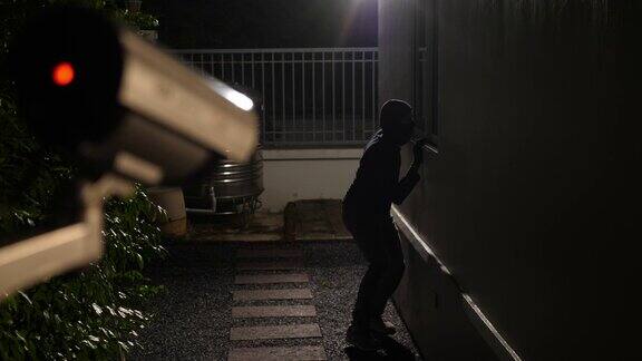 闭路电视监控摄像头捕捉到小偷在晚上跳下来试图进入一所房子的场景