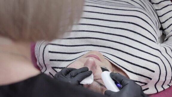 美容师美容师用超声波刮刀给年轻女性做面部护理用超声波刮刀洗脸美容院的面部清洁程序