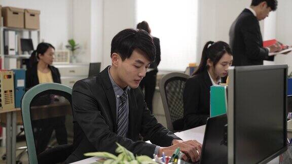 集中的亚洲商人穿着西装在公司明亮的办公室里与同事们一起在笔记本电脑上工作