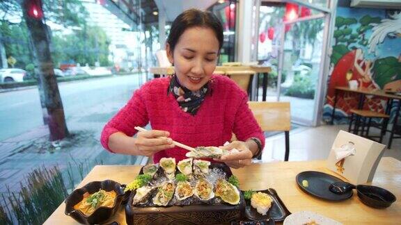 亚洲妇女在日本餐厅吃新鲜的生蚝在日本料理中用餐