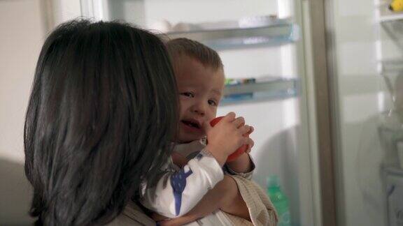 亚洲妈妈抱着婴儿从冰箱里拿出一个西红柿