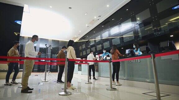 低角度的亚洲华人观众在售票柜台前排队购买电影票和爆米花饮料在电影院放映前进行非接触式支付