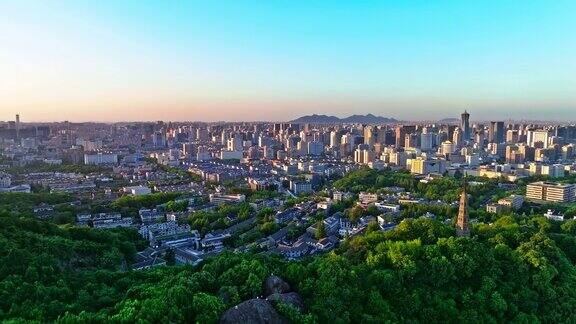 鸟瞰中国浙江省杭州市日落时分的城市和绿色山景的现代建筑