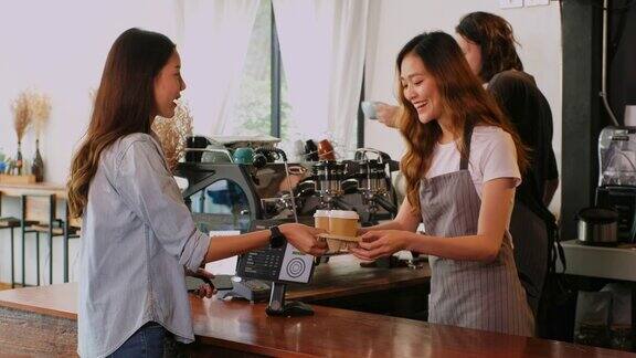 年轻的亚洲女咖啡师咖啡馆老板在咖啡馆柜台为顾客提供外卖咖啡的女服务员