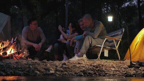 快乐的亚洲大家庭享受在森林篝火附近的夜晚露营采购产品家庭生活方式人老年人假期关系假期退休保健和医学概念东南亚及东亚:世代家庭、篝火