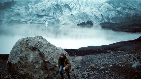 年轻英俊的男子坐在冰泻湖的岩石上看着冰岛的冰川游客站起来走开