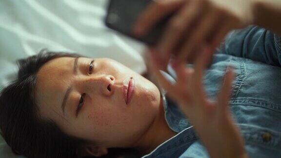 年轻女子躺在床上使用智能手机的高角度照片