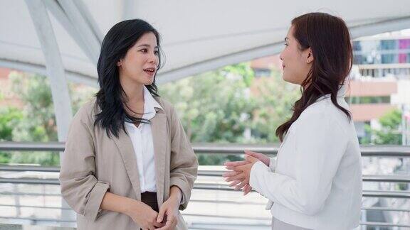 快乐自信的亚洲商务女性与合作伙伴交谈并握手同时接受业务交易户外会议在办公大楼区域
