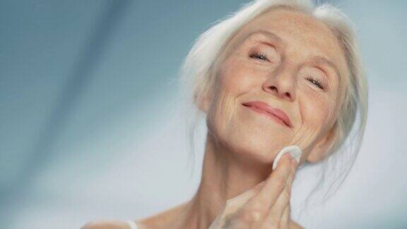 中等画像:美丽的老年妇女用棉花垫清洁她完美的脸上的化妆品微笑的老妇人与柔软的皮肤优雅的老年及天然护肤洁面产品