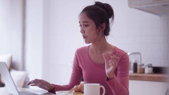 年轻快乐的亚洲自由职业女性早餐吃牛角面包喝咖啡在厨房柜台上用笔记本电脑工作享受在家工作