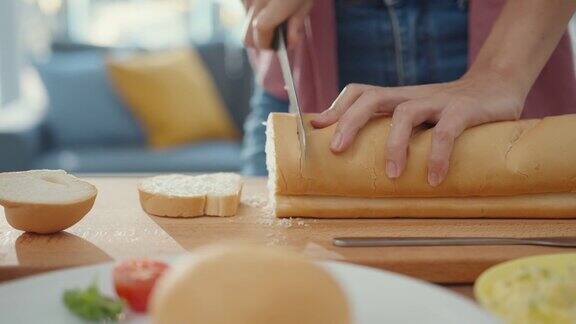 年轻的亚洲女厨师双手握着刀在厨房桌子上的木板上切着全麦面包