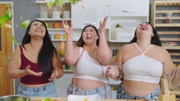 一群快乐的胖乎乎的女性朋友向空中扔蔬菜三个亚洲大码女人把蔬菜扔向空中对自己的身体很有信心健康食物概念