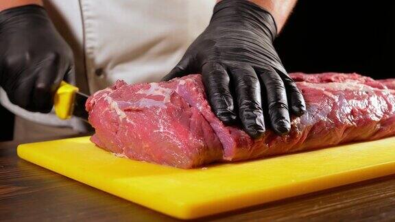 一位戴着黑手套的职业屠夫用一把锋利的刀从肠内切下一片生肉做牛排厨师在烤架上为烹饪做准备