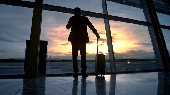 日落时分一个商人走到机场的玻璃墙前打电话