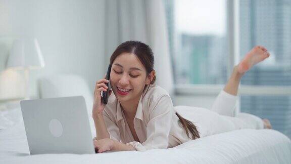 亚洲女商人使用科技平板电脑工作在床上通过智能手机打电话