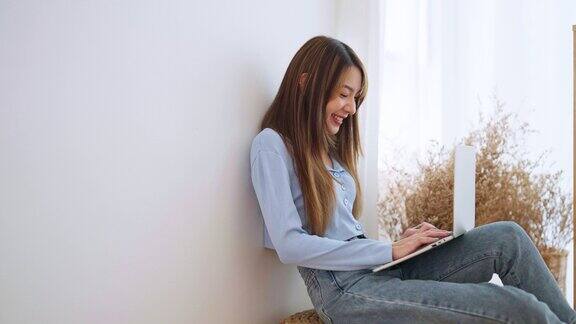 年轻的亚洲女性在家工作快乐的女性在家里的客厅里使用笔记本电脑