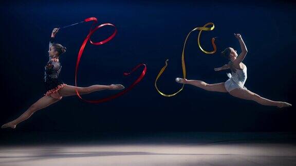 SLOMOSPEEDRAMPLD两名艺术体操运动员向相反的方向移动并在旋转丝带的同时表演分裂跳跃