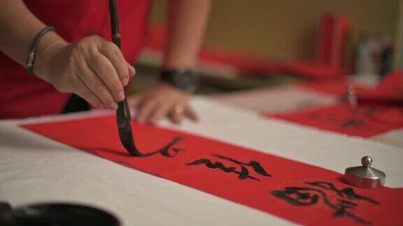 亚洲华人男性练习书法的手为即将到来的中国新年庆祝家庭装饰目的繁荣和良好的措词写在一张红色的纸上
