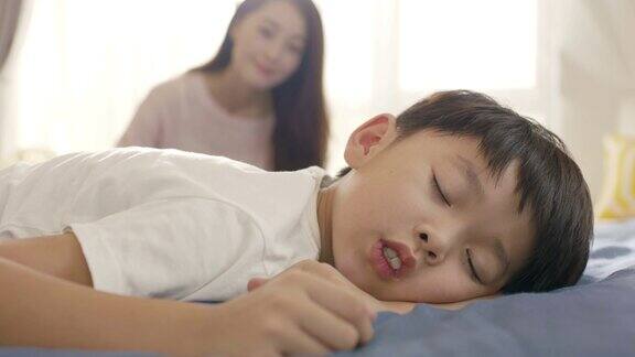 年轻的亚洲母亲微笑着在早晨叫醒她的儿子的特写