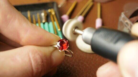 一个专业的珠宝商用一种特殊的工具打磨金戒指上的红色宝石这位珠宝商正忙着把一块宝石镶在金戒指上