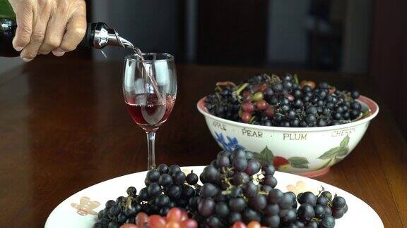 男子把红酒倒进木桌上的酒杯里用陶瓷盘子和碗盛着刚收获的葡萄