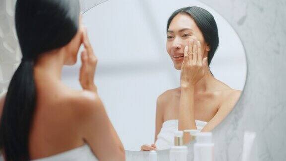 美丽的亚洲妇女肖像轻轻应用面霜面膜感性的触摸看在浴室的镜子年轻女性使她的皮肤柔软清洁与天然化妆品护肤品