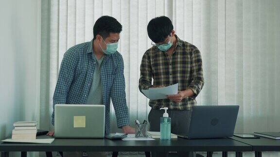 一位亚洲同事戴着口罩站在办公室分析企业数据