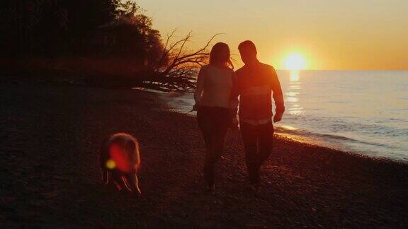 一对浪漫情侣的剪影日落时分在湖边或海边遛狗