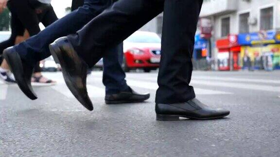 两个商人的脚走在城市街道上商人正在过街自信的人正在去办公室的路上同事的腿在户外慢动作近景低角度视图
