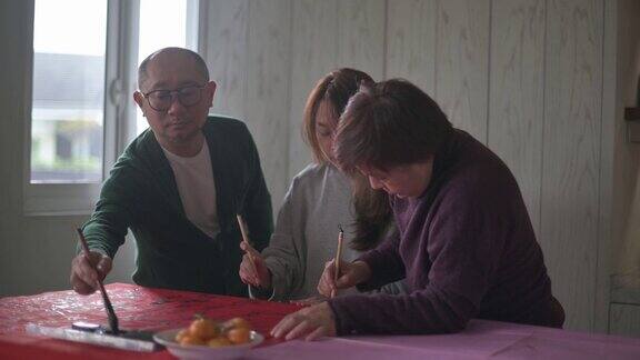 亚洲华人家庭在红纸上书写中国书法以求繁荣准备中国新年的家庭装饰