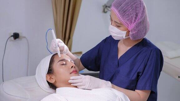 美容医师在病人前额皮肤上做真皮针刺治疗亚洲年轻美丽女性在脸上做微针光疗收紧、提升、恢复肌肤活力