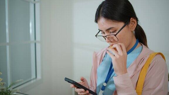 穿着制服的年轻女医生在家里使用智能手机和吃饼干