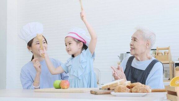 可爱的小女孩与年轻的母亲和老妇人在厨房里快乐地跳舞