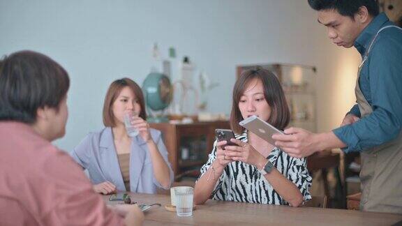 亚洲华人妇女使用手机应用支付账单在咖啡馆服务员与移动支付方式