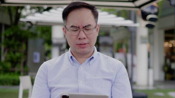 亚洲中年男子戴着眼镜在外面用笔记本电脑进行视频通话研讨会与同事使用视频会议应用视频通话虚拟交流娱乐在线